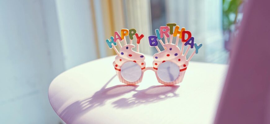 привітання з днем народження свекрусі — Colorful birthday glasses with 'Happy Birthday' sign on a pink chair in bright sunlight. | ITmaxService