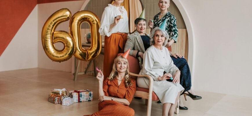 Щирі привітання з ювілеєм жінці — Five senior women celebrating a 60th birthday with party hats and balloons indoors. | ITmaxService