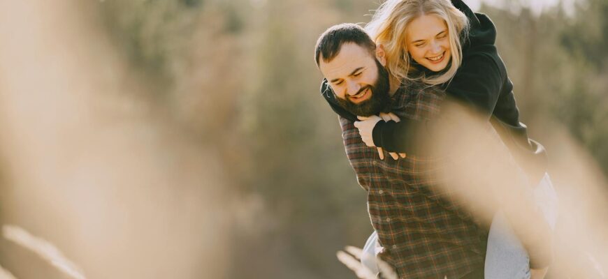привітання коханому з днем народження — Positive piggyback couple in warm casual wear hugging and having fun while spending weekend together in countryside in sunny morning | ITmaxService